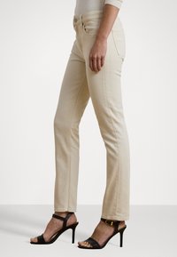 Beige rette benklær med en glatt tekstur og strukturert passform, kombinert med svarte strappy høyhælte sandaler.
