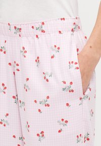 Pantaloni a quadri rossi e bianchi di un delicato rosa chiaro, con una vita elasticizzata e stampati con fragole rosse e fiori bianchi. Inclusi tasche laterali.