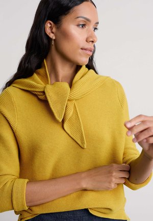 Senfgelber, gerippter Pullover mit einem einzigartigen Knoten-Detail am Ausschnitt, ausgestattet mit langen Ärmeln und einem lockeren Schnitt.