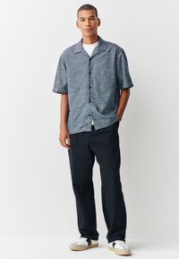 Korte mouwen overhemd met knopen, gemaakt van gestructureerde marineblauwe stof, met een campkraag en zwarte knopen, gecombineerd met donkere broek en casual sneakers.