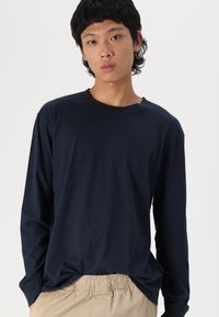 Navy long-sleeve t-shirt made of cotton, featuring a relaxed fit and crew neckline, paired with light beige, elastic-waist pants.