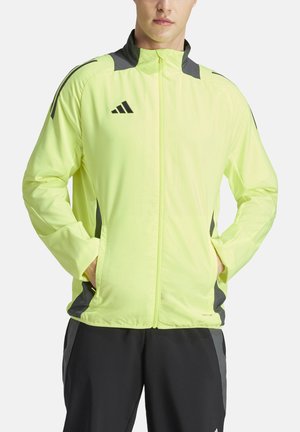 Neon gele sportjack met grijze accenten, lichte stof, volledige rits en zijzakken. Beschikt over een opstaande kraag en logodetail.