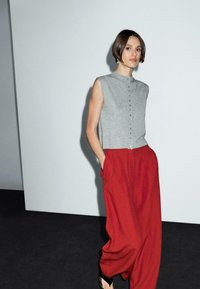 Grå ärmlös topp med knappar, parat med lösa röda byxor. Outfiten har ett mjukt tyg och en avslappnad passform, kompletterad med enkla svarta sandaler.