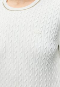 Pull blanc en tricot torsadé avec un col rond et un logo brodé subtil sur la poitrine.