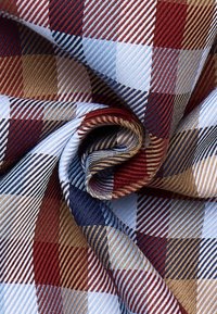 Katoenen stof met een multikleurig ruitpatroon in rode, blauwe en beige tinten, met een gestructureerde diagonale weving en glanzende afwerking.