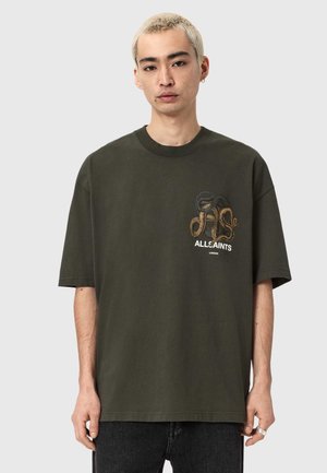 T-shirt oversize verde oliva in cotone, con un design di serpente in nero e oro, e un logo stampato in basso.