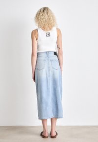 Denim midi suknja u svijetloplavoj boji, s visokim strukom, dva stražnja džepa i glatkom teksturom tkanine. Uparena s bijelim topom bez rukava.