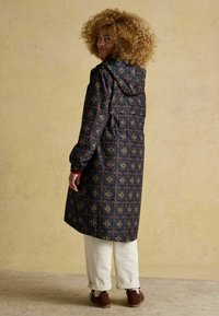 Garšs kapuci mētis tumšā audumā ar ģeometrisku rakstu zeltā, sarkanā un zilā krāsā. Elastīgās piedurknes un savilktā josta uzlabo piegulšanu.