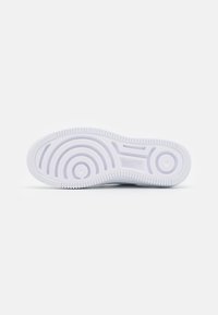 Semelle de basket blanche avec un motif de bande de roulement ondulé, des bords en caoutchouc texturé et des rainures circulaires pour une meilleure adhérence et traction.