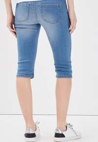 Pantaloni capri in denim di colore azzurro chiaro, con una forma aderente, orli arrotolati e due tasche posteriori. Abbinati a sneaker bianche e argentate.