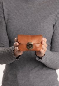 Smeđa kožna torbica zaokruženog oblika, s preklopom i brončanim kopčom. Glatka tekstura s vidljivim detaljima šivanja.