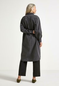 Lång, mörkgrå skjortklänning av mjukt tyg med krage, knappade manschetter och rynkade ärmar, tillsammans med mörka byxor.