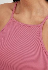 Rosa ribbad linne med tunna axelremmar och rund halsringning, tillverkat av ett mjukt, stretchigt material för en figurnära passform.