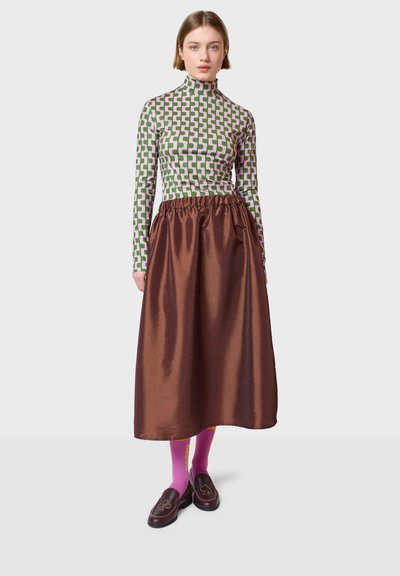 Duga majica s turtleneckom s geometrijskim uzorkom u zelenoj i ružičastoj boji, uparena s sjajnom smeškastom suknjom, ružičastim čarapama i tamnim lofericama s detaljem u akcentu.