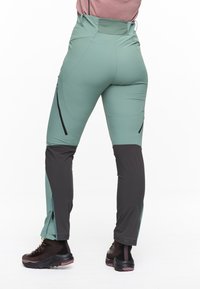 Grüne und schwarze Outdoorhosen mit Reißverschlusstaschen, taillierte Passform und glatter Textur. Mit Reißverschlüssen an den Knöcheln für Belüftung.