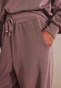 Mauve jogginghousut pehmeästä kankaasta, jossa on joustava vyötärö, naru, sivutaskut ja rento istuvuus. Sujuva tekstuuri ja yksinkertainen muotoilu.