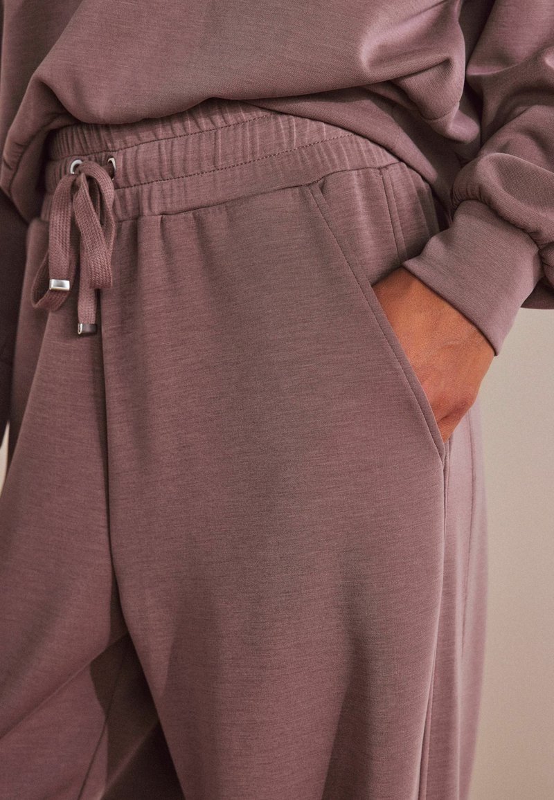 Mauve jogginghousut pehmeästä kankaasta, jossa on joustava vyötärö, naru, sivutaskut ja rento istuvuus. Sujuva tekstuuri ja yksinkertainen muotoilu.