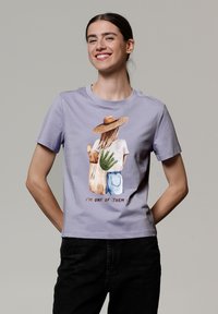 Lavendel katoenen T-shirt met een grafiek van een figuur met een strohoed, die een aloëplant en een totebag vasthoudt, tekst: "IK BEN ER EEN VAN."