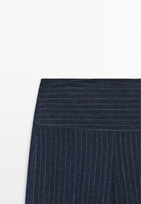 Tissu bleu foncé avec fines rayures blanches verticales et horizontales, montrant une section de couture pliée.