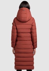 Lange, gewatteerde jas in roestkleur met een grote capuchon. Heeft horizontale doorgestikte delen en een nauwsluitende taille, eindigend onder de knie.