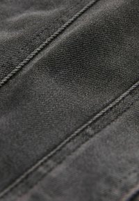 Black denim fabric showing a textured surface with diagonal stitching lines, highlighting a worn appearance and soft finish.