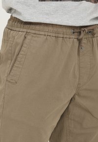 Pantalon de jogging kaki avec taille élastique et cordon de serrage, doté de poches latérales et d'un tissu doux et texturé.