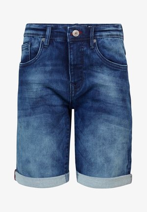 Dreng står iført en sort t-shirt med tekst, op rullede denimshorts, hvide sokker med sorte striber og sorte sneakers med hvide snørebånd.