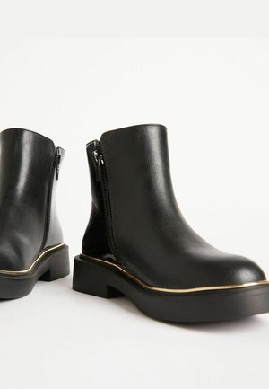 Schwarze Leder-Stiefeletten mit seitlichen Reißverschlüssen, robusten Sohlen und einer dünnen Metallverzierung entlang der Sohlenkante, auf einem weißen Hintergrund.