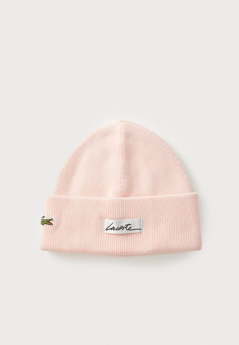 Lys rosa ribbet strikket lue med brett, med en liten grønn krokodille-logo og en hvit rektangulær etikett med svart kursiv tekst.