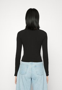 Camisa preta de mangas longas com um design ajustado, decote redondo e mangas raglan, combinada com jeans de perna larga de cor azul clara que possuem bolsos traseiros.