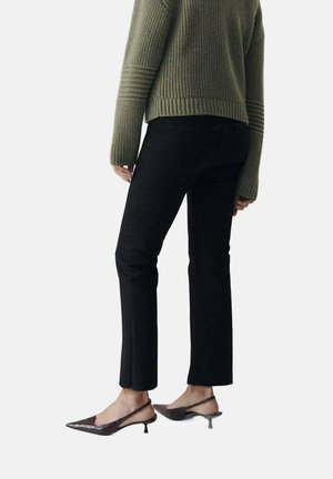 Black jeans with a straight cut and slight fray at the hem, paired with an olive green ribbed sweater and brown pointed-toe heels.