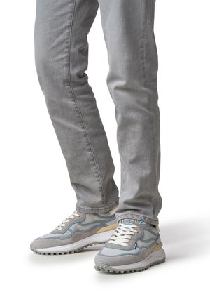 Grijze spijkerbroeken gecombineerd met lichtblauwe en grijze sneakers met een bovenwerk van gemengd materiaal, opvallende veters en een gestructureerde rubberen zool.