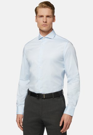 Camicia da uomo a maniche lunghe di colore blu chiaro con colletto a punta, chiusura a bottone e polsini, abbinata a una cintura nera e pantaloni grigi sartoriali.