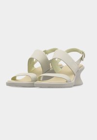 Μπεζ ανοιχτά σανδάλια με λουράκια στο πίσω μέρος και χαμηλά τακούνια τύπου πλατφόρμας, με μοντέρνο, μίνιμαλ σχεδιασμό σε λευκό φόντο.