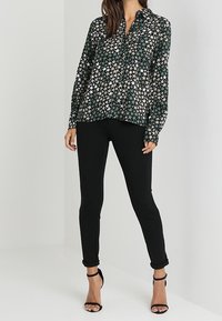 Blusa de manga larga con una base verde oscura y un patrón de estrellas en blanco y beige; combinada con pantalones skinny negros y tacones negros de tiras.