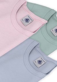 Trois hauts sans manches en coton de couleur rose, vert menthe et bleu clair. Chacun présente un col arrondi avec une bordure texturée et une étiquette.