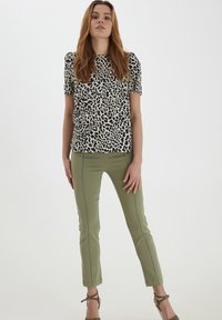 Haut à manches courtes avec un imprimé léopard noir et crème, associé à un pantalon olive ajusté avec des détails de couture. Talons verts à bout fermé.