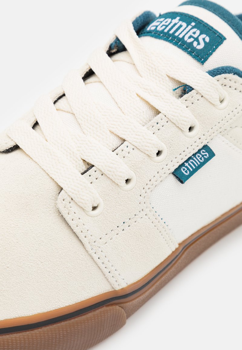 Weißer Sneaker aus leichtem Wildleder und Canvas-Materialien, mit blauem Etnies-Logo, cremefarbenen Schnürsenkeln und Gummisohle.