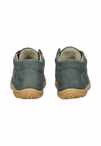Bottines en daim gris avec une semelle en caoutchouc flexible de couleur tan, dos arrondi et détail de couture. Doublure en cuir doux visible à l'ouverture.