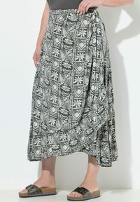 Jupe à motifs noir et blanc avec une bordure volante, fabriquée en tissu léger ; présente des motifs floraux et géométriques. Portée avec des sandales à enfiler.
