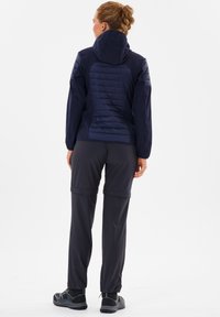 Marinehættejakke med teksturerede paneler, parret med mørke bukser. Outfittet har justerbare manchetter og praktisk fodtøj.