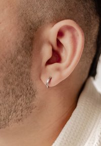 Orecchino a cerchio in argento appeso a un orecchio maschile, con una superficie liscia e lucida e un semplice design circolare. Inquadratura ravvicinata del lobo dell'orecchio.