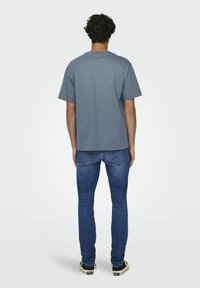 Grijze T-shirt met korte mouwen en een relaxte pasvorm, gecombineerd met blauwe jeans. Het T-shirt heeft een ronde hals en een zachte textuur.