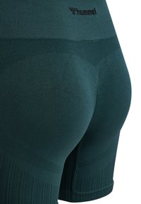 Mørkegrønne træningsshorts i tekstureret stof med ribbede detaljer og det sorte "hummel"-logo nær taljebåndet.