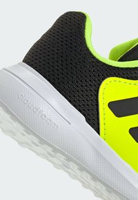 Black and neon yellow athletic shoe with a mesh upper, smooth accents, and a white rubber sole featuring textured grip patterns.
