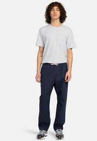 Grå bomulds t-shirt med brystlomme, parret med marineblå joggerbukser med snoretræk og sorte sneakers med multicolore accenter.