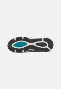 Semelle de chaussure de sport noire et blanche avec une section turquoise et adhérence texturée, vue de dessous sur fond blanc uni.
