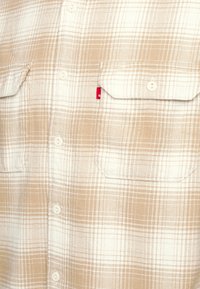 Camicetta a quadri beige e bianca realizzata in morbido tessuto, con due tasche sul petto, apertura con bottoni e un piccolo logo rosso Levi's.