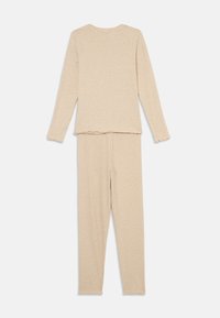 Beige långärmad topp och matchande byxset, tillverkat av mjukt tyg med fransade kanter, med en enkel design och figurnära silhuett.