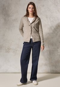 Ljusgrå stickad cardigan med huva, knäppning fram och ribbade muddarna, ihop med mörkblå vida jeans och vita sneakers.